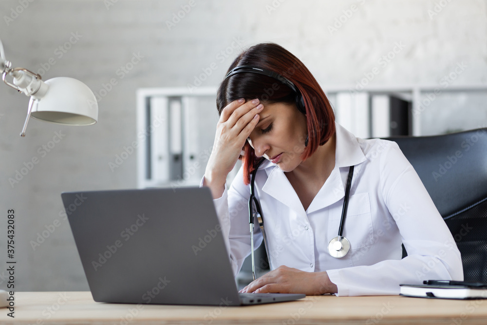 Woman Doctor is tired of consultations. Online medical assistance. Challenging work in a pandemic. Medical worker's headache. Woman Doctor is tired of consultations. Online medical assistance. Challenging work in a pandemic. Medical worker's headache.