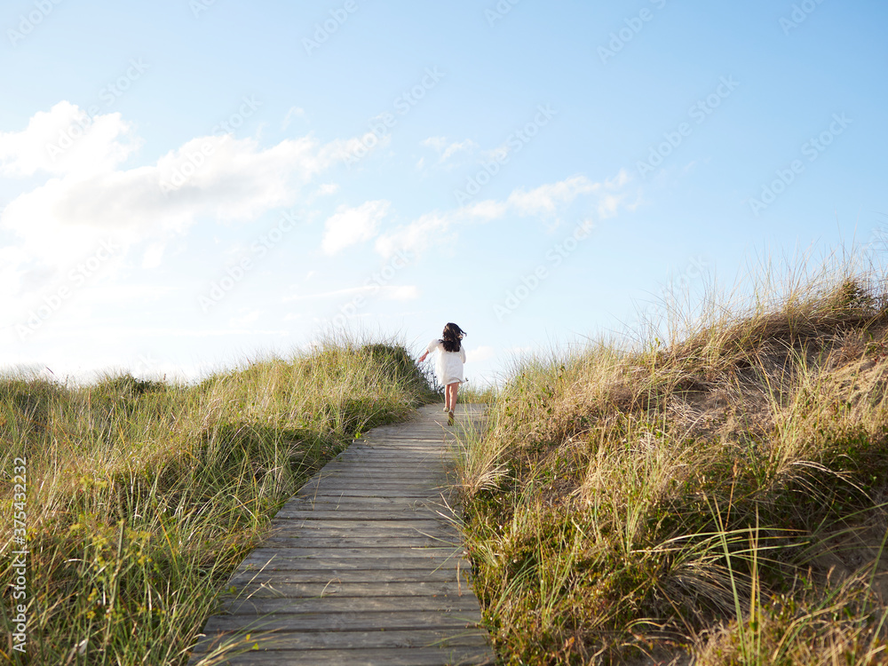 Obraz premium Niña corriendo en pasarela de madera en la playa