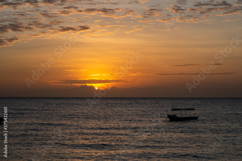 Orange sunset over the Indian Ocean on the coast of Pemba Island  Tanzania  with low clouds on the horizon and silhouette of a fishing boat.