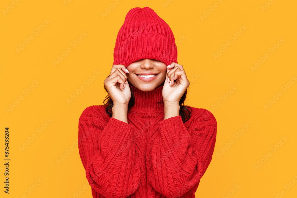 Cheerful ethnic female pulling hat on eyes.