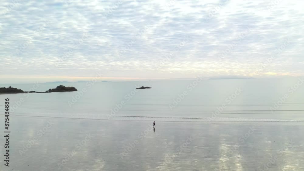 Person walking alone on empty coastal bay beach at sunset, aerial arc shot Person walking alone on empty coastal bay beach at sunset, aerial arc shot