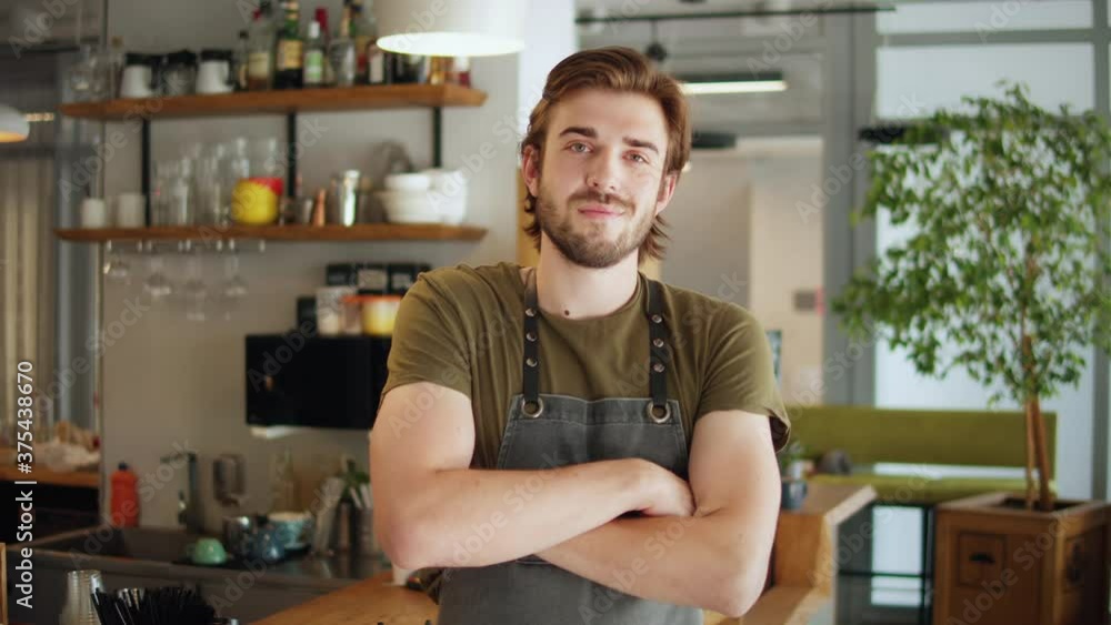 Successful small business owner standing with crossed arms with employee in background preparing coffee Successful small business owner standing with crossed arms with employee in background preparing coffee