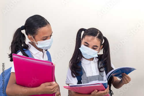 Schoolgirls wearing medical mask looking to the notebook. School during coronavirus infection. Little girls studying.