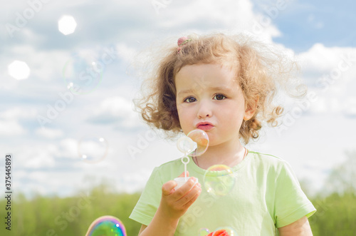Little beautiful girl blows soap bubbles. Cute baby enjoys outdoor games. happy summer child in nature.