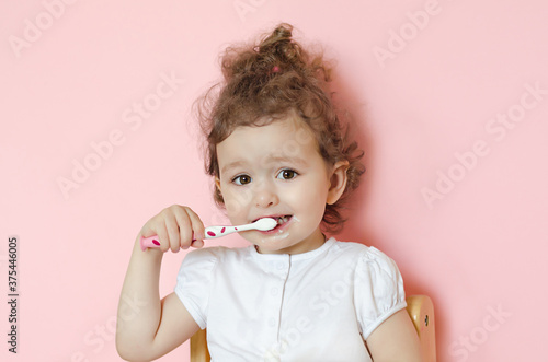 little beautiful girl 3 years old brushing her teeth on pink background. baby learns oral hygiene.