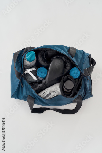 Boxing equipment for everyday training. Top view of a sports bag with boxing gloves, hand wraps, clothing, bottle of water and etc isolated on grey background