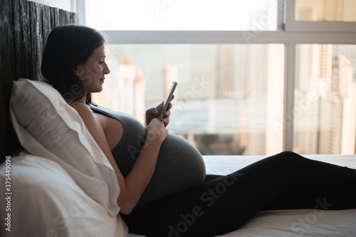 Pregnant woman using mobile phone on bed (ID: 375449098)