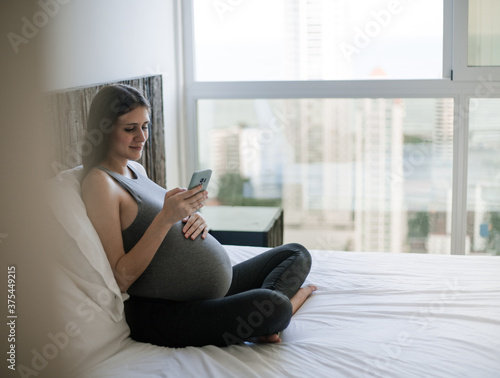 pregnant woman sitting on bed and view phone (ID: 375449215)