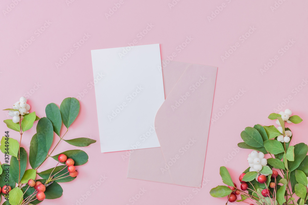 Mockup white greeting card and envelope with green leaves, flowers and small red apples on a pink background Mockup white greeting card and envelope with green leaves, flowers and small red apples on a pink background