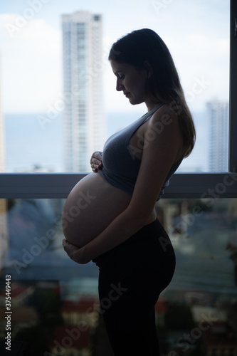 pregnant woman on the windows building - pregnancy concept (ID: 375449443)
