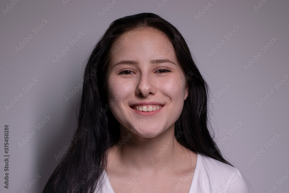 Indoor portrait of Beautiful smiling brunette with clean skin, natural make-up. smiling cheerfully, feeling happy and carefree. cosmetic concept. young model with beautiful smile on grey background Indoor portrait of Beautiful smiling brunette with clean skin, natural make-up. smiling cheerfully, feeling happy and carefree. cosmetic concept. young model with beautiful smile on grey background