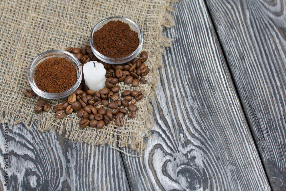 Coffee beans on rough linen and candle stub. Ground coffee in containers. On a surface of brushed pine boards painted black and white. Coffee beans on rough linen and candle stub. Ground coffee in containers. On a surface of brushed pine boards painted black and white.