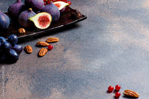 Fresh ripe figs on dark plate with truffle candy, red currant, blue grape and pecan nuts, copy space