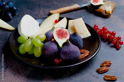 Figs, cheese, grapes, pears and mozzarella with red current on dark plate, closeup