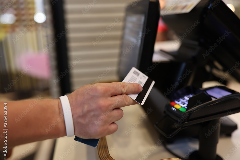 Man's hand holds a plastic card in his hands and applies it to terminal. Safe payments by bank cards concept Man's hand holds a plastic card in his hands and applies it to terminal. Safe payments by bank cards concept