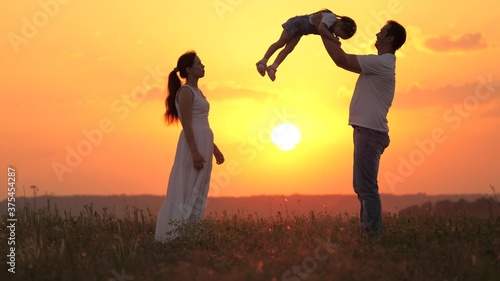 dad plays with his little daughter  happy to throw child into air  happy mom admires her family. mommy daddy and baby  family is resting at sunset in field. happy healthy family walking in fresh air.