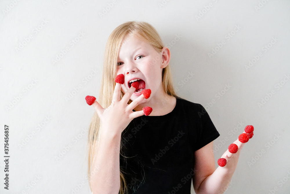 Girl with a big raspberry on her fingers. Happy child eating berries Girl with a big raspberry on her fingers. Happy child eating berries