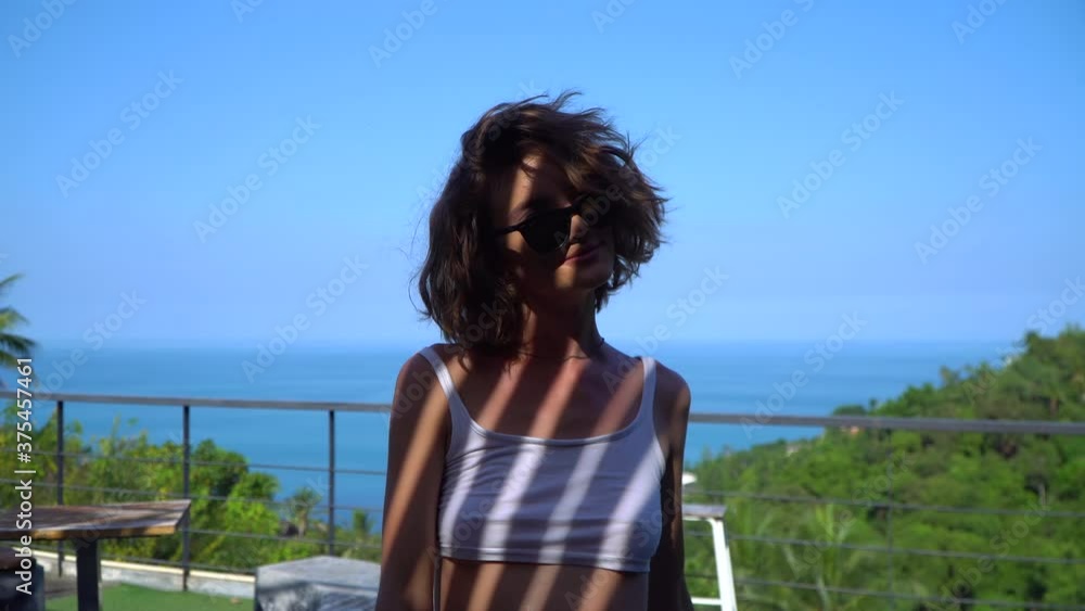 The brunette looks at the camera, a shadow falls on her face, waves her head, plays with her hair in a white short t-shirt and black glasses, smiles 4K The brunette looks at the camera, a shadow falls on her face, waves her head, plays with her hair in a white short t-shirt and black glasses, smiles 4K