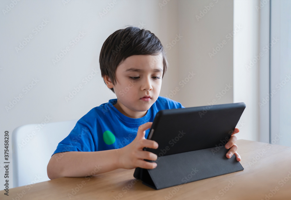 New normal, Kid using tablet studying homework, Child using digital tablet for his online lesson at home during quarantine, Home schooling, Social Distancing and E-learning online education concept New normal, Kid using tablet studying homework, Child using digital tablet for his online lesson at home during quarantine, Home schooling, Social Distancing and E-learning online education concept