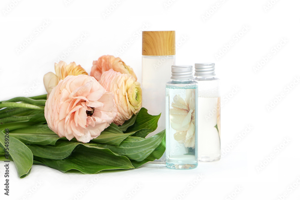Reusable bottles with liquid on yellow pink ranunculus flowers and green leaves background Reusable bottles with liquid on yellow pink ranunculus flowers and green leaves background