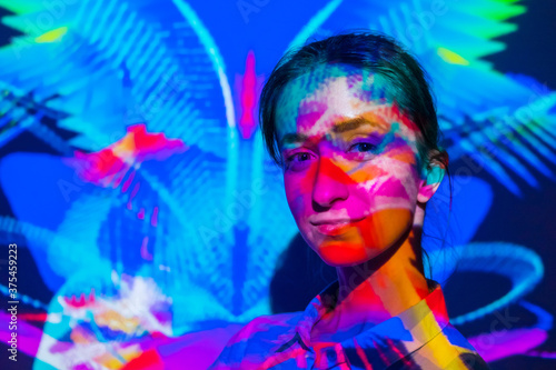 Colorful portrait of woman in plaid shirt at modern immersive exhibition or club party with dynamic projector multicolor light illumination. Digital art and entertainment concept photo