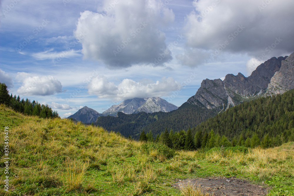 Beautiful summer mountain landscape. Col di San Piero meadow framed by woods and mountains under the cloudy sky. Domegge di Cadore, Belluno, Italia