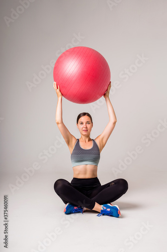 girl athlete sits and holds a large red fitness ball on a white isolated background with space for text © Яна Айбазова