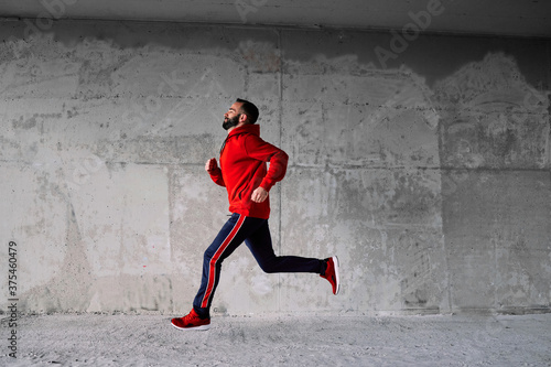 Side view of attractive fit sportsman in red tracksuit running fast.