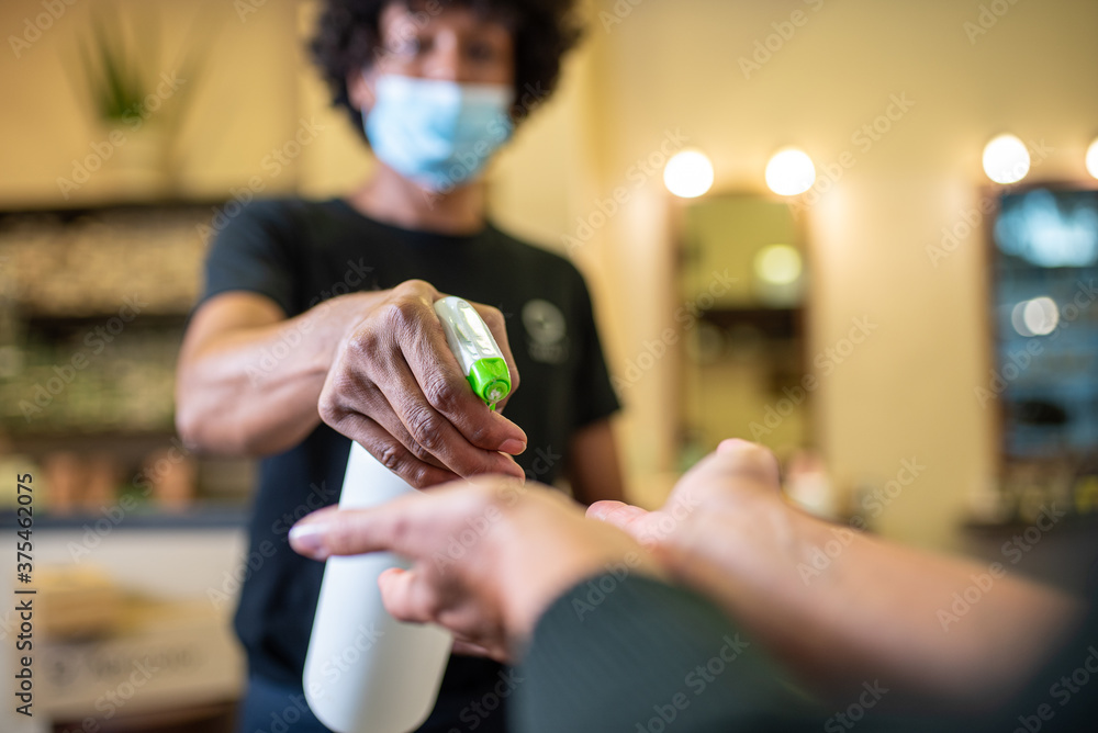 hand sanitization operation at the entrance of a business, a store clerk sprays disinfectant on a customer's hands, prevention actions in coronavirus outbreak