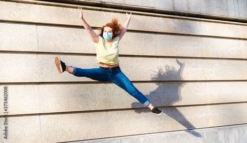 red head young girl of the Z generation wearing a lprotective mask does an acrobatic jump with open legs, concept of positive thinking and optimism in time of covid19 outbreak