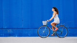 Woman in a white dress  riding a bike in the city on a blue wall. Sustainable mobility, urban cyclist