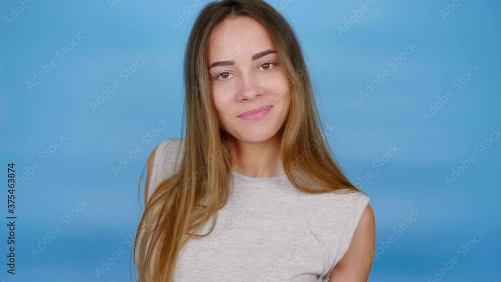 Beautiful woman with long hair in gray t-shirt is dancing on blue background with copy space. 4K slow motion footage Beautiful woman with long hair in gray t-shirt is dancing on blue background with copy space. 4K slow motion footage