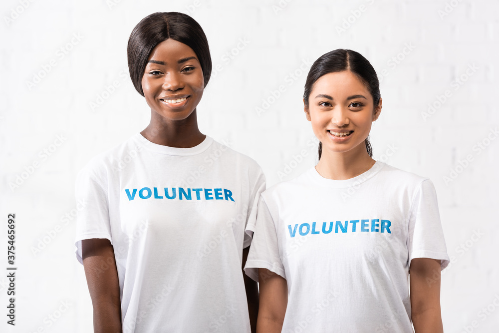 Asian and african american women with volunteer lettering on t-shirts looking at camera Asian and african american women with volunteer lettering on t-shirts looking at camera