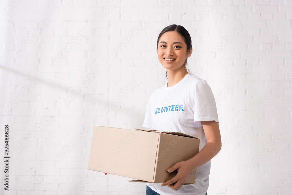 Young asian volunteer with cardboard box looking at camera in charity center Young asian volunteer with cardboard box looking at camera in charity center
