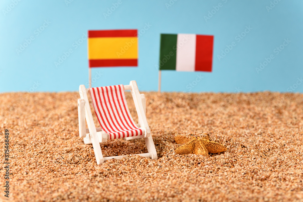 Sunbed on the beach with Spanish, Italian flag on the blurred background. Sunbed on the beach with Spanish, Italian flag on the blurred background.