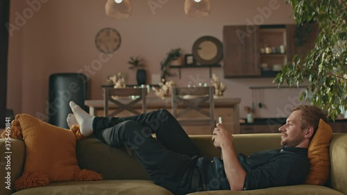 A man lies on a sofa and uses a smartphone. Cozy Living Room