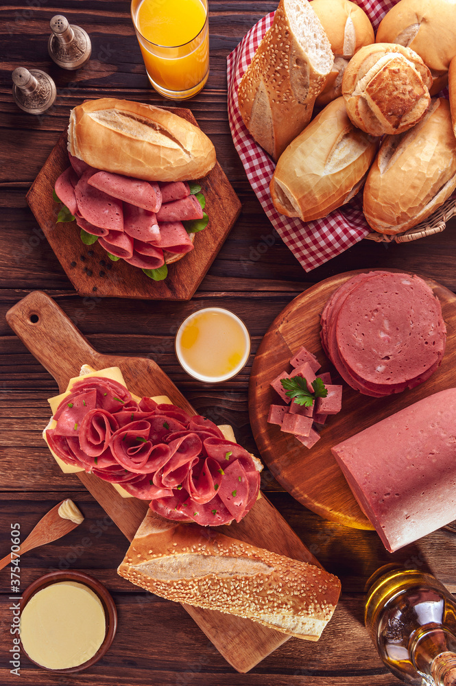 Mortadella sandwich with orange juice, bread, butter and spices on wood background - Top view