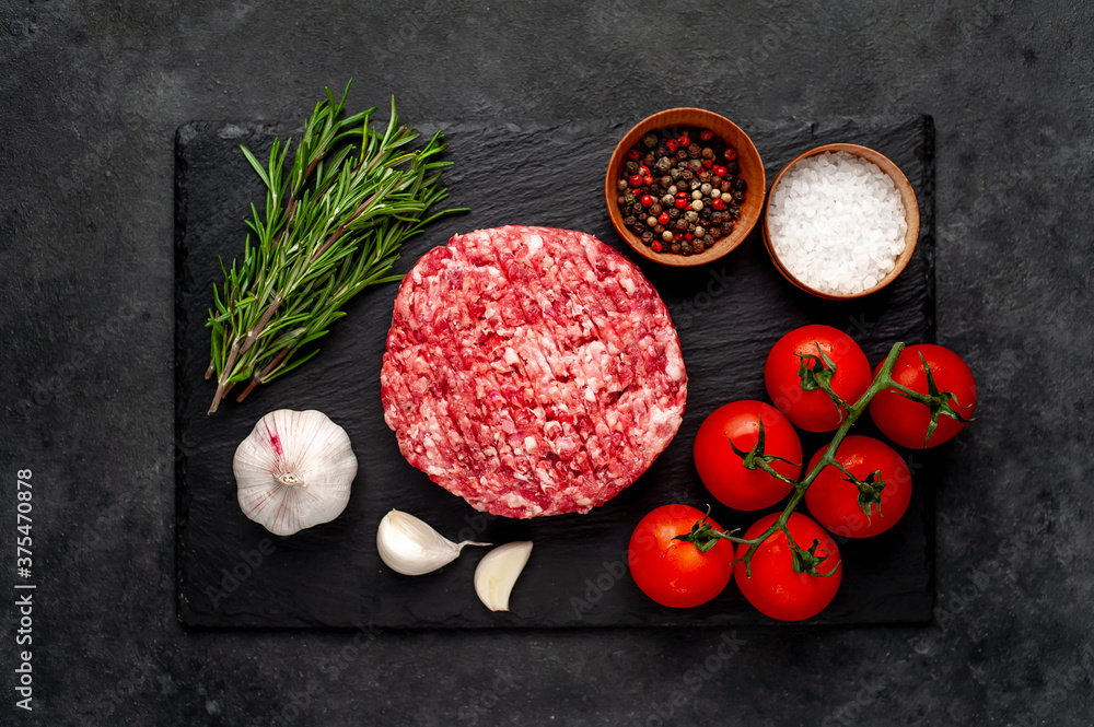 Raw beef burger cutlets with rosemary and spices on a slate board on a concrete background Raw beef burger cutlets with rosemary and spices on a slate board on a concrete background