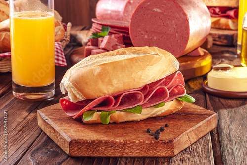 Fotografija Mortadella sandwich with orange juice, butter and piece of mortadella on wood ba