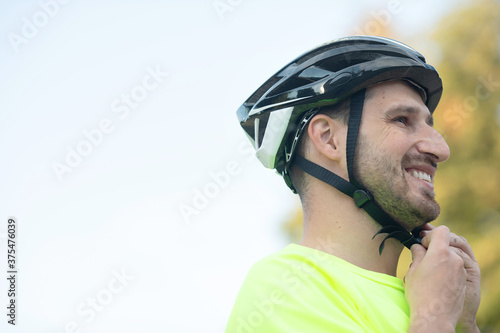 Handsome young man putting on bicycle helmet in park. © lashkhidzetim