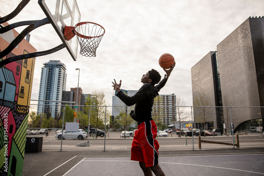 Foto Stock Young man shooting hoops on urban basketball court with mural |  Adobe Stock