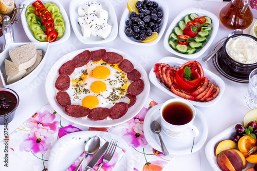 Traditional Turkish Breakfast with tomato,olives,honey,tea,cheese and egg with sausage on white surface.