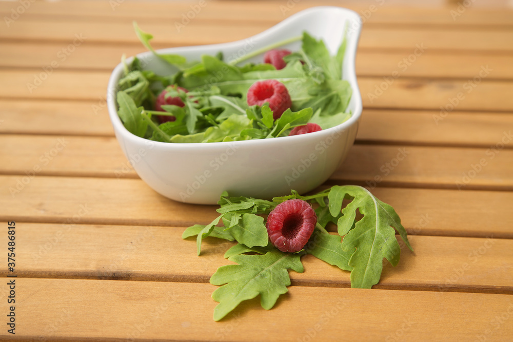 white deep dish with fresh arugula and raspberries. The concept of healthy food white deep dish with fresh arugula and raspberries. The concept of healthy food