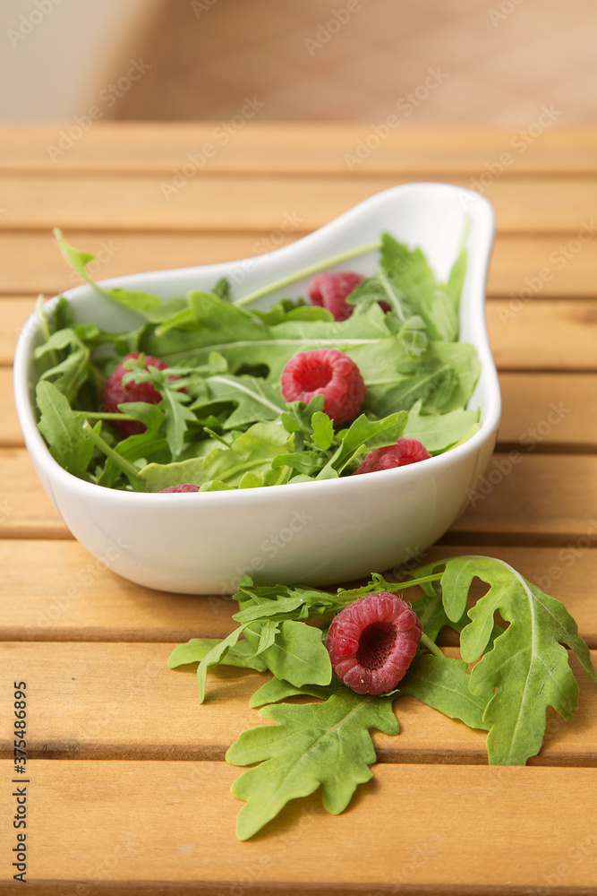 white deep dish with fresh arugula and raspberries. The concept of healthy food white deep dish with fresh arugula and raspberries. The concept of healthy food