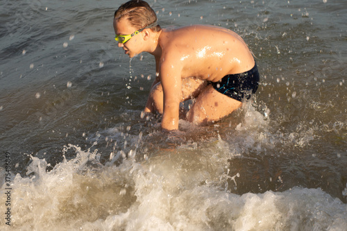 Fototapeta Naklejka Na Ścianę i Meble -  A 10-year-old boy in green swimming goggles swims in the sea near the shore.