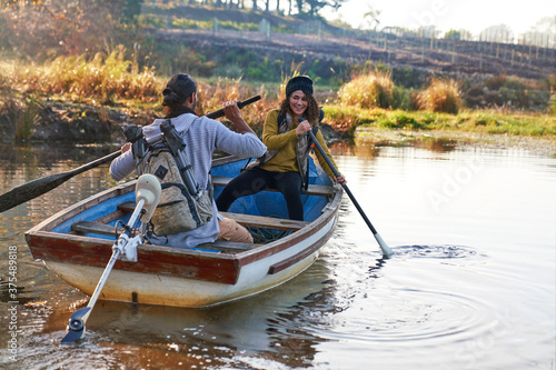 Happy young couple with oars in rowboat on sunny autumn lake
