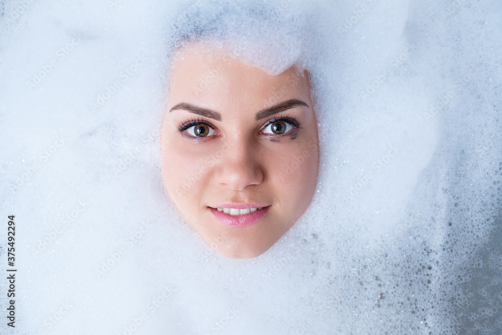 Closeup portrait of a girl in a bathtub and white foam around her face. Different emotions, grimaces, woman smile Closeup portrait of a girl in a bathtub and white foam around her face. Different emotions, grimaces, woman smile