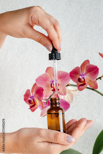 Young woman holds an essence for skin in her hands. Tropical orchid flowers. Unisex cosmetics. Place for text. Spa natural organic products. Anti-age cosmetics for men and women. 