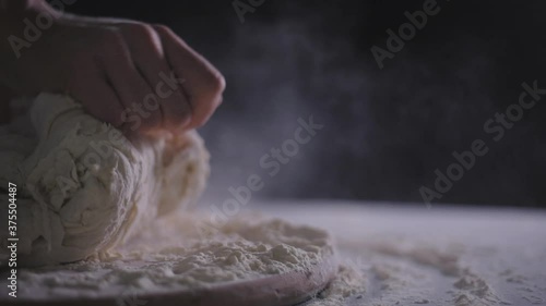 Close up view of baker kneading dough in flour on table. Hands of female chef kneading floured dough for bread.