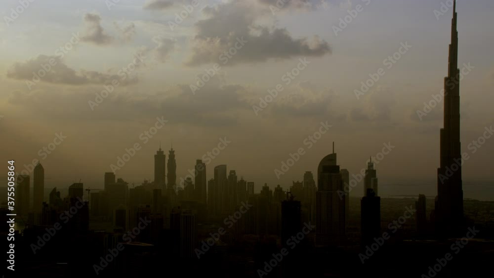 A beautiful silhouette aerial view of Burj Khalifa and neighboring skyscrapers creating a vast shadow of the sun over the city, 6-axis stabilized gimbal, Shotover F1, 8K, parallax. A beautiful silhouette aerial view of Burj Khalifa and neighboring skyscrapers creating a vast shadow of the sun over the city, 6-axis stabilized gimbal, Shotover F1, 8K, parallax.
